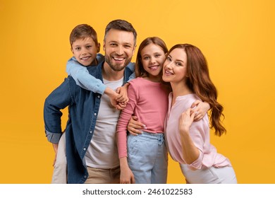 A cheerful family consisting of a father, mother, boy, and girl closely huddled together, sharing a warm embrace while flashing bright smiles against a vibrant yellow backdrop