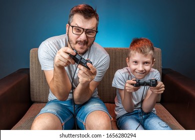 A Cheerful Family, Dad And Son Play On The Console, In Video Games, Emotionally React While Sitting On The Couch. Day Off, Entertainment, Leisure, Spend Time Together