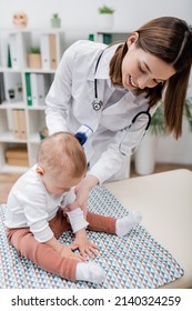 Cheerful Family Doctor Holding Pyrometer Near Baby On Medical Couch In Clinic