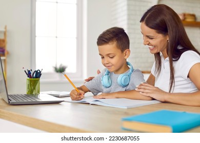 Cheerful family doing school assignment at home. Happy young mother sitting at desk together with her son, helping him with homework, smiling and supporting him. Children, education concept - Shutterstock ID 2230687055