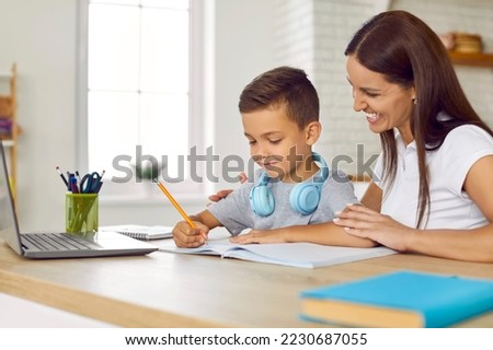 Cheerful family doing school assignment at home. Happy young mother sitting at desk together with her son, helping him with homework, smiling and supporting him. Children, education concept Stock photo © 