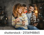 A cheerful family enjoy online shopping, parents and son smile as they share a moment of togetherness while holding a credit card in a cozy setting