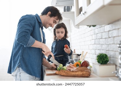 Cheerful family father dad with little small child daughter preparing vegetable salad at home, cooking family dinner for celebrating father`s day. Daughter helping his dad cook lunch. Fatherhood - Powered by Shutterstock