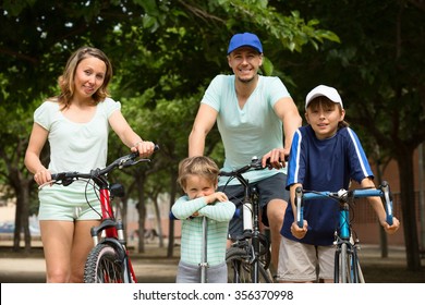 cheerful family of four with bicycles  walking in park