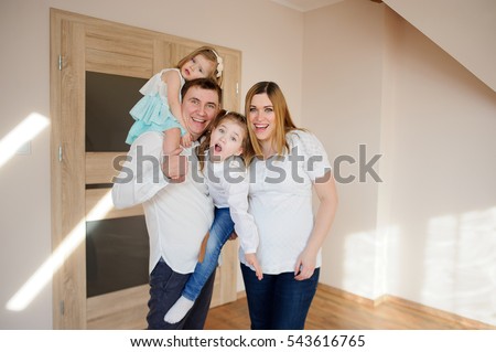 Cheerful family of four people. Young man holding in his arms his two daughters. Pregnant wife snuggles on husband. All great fun.