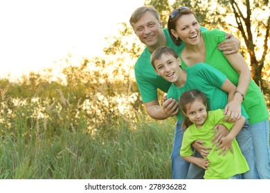 Cheerful Family In Green Shirts Walking In The Summer Park