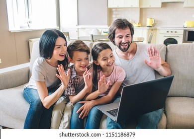 Cheerful Family Has Laptop And Waves With Their Hands. They Talk On Skype. Pretty People Are Smiling.