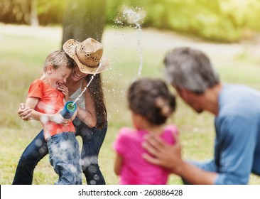 Cheerful Family Having Fun She Does A Water Gun Fight, Mom And Son Against Dad And Daughter, Focus On Mom And Her Son