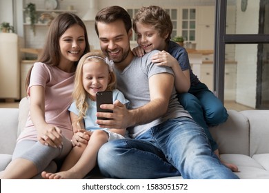 Cheerful family with little kids seated on sofa play new game on smartphone, take selfie photo having fun on-line using app, make video call talk with relatives, buying distantly e-commerce concept - Powered by Shutterstock