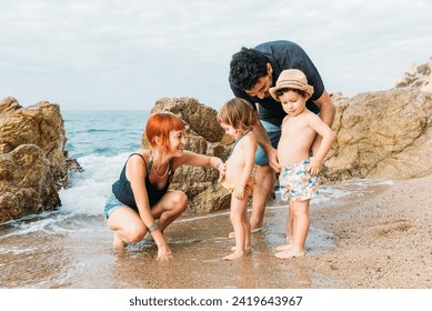 Cheerful family with little toddler kids having fun together on rocky seashore near waving ocean in daytime and enjoying vacation - Powered by Shutterstock