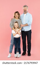 Cheerful Family Of Middle Aged Parents And Little Daughter Embracing Smiling To Camera Standing Over Pink Studio Background. Happy Parenting Concept. Vertical Shot, Full Length