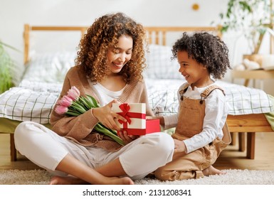 Cheerful Family Mom Opens A Gift Box With Her Son And Holding Bouquet  Of Flowers While Resting On Floor By Bed During Holiday Celebration Mothers Day At Home