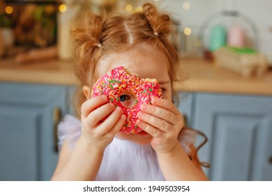 A Cheerful Family On The Background Of A Bright Kitchen. Daughter Girl Have Fun With Colorful Donuts. He Looks Through The Hole In The Doughnut Near His Eyes.