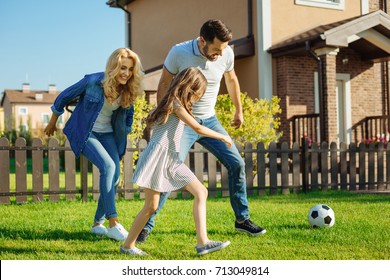 Cheerful Family Playing Football On The Backyard Lawn