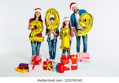 Cheerful Family In Santa Hats Holding Golden Numbers 2019 And Gift Boxes On White Background. Happy New Year Party