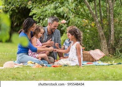 Cheerful family sitting on the grass during a picnic in a park, there is a basket with meal and toys for the kids