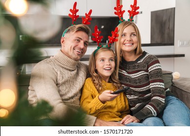 Cheerful family sitting together on a couch at the living room on a Christmas eve, watching tv