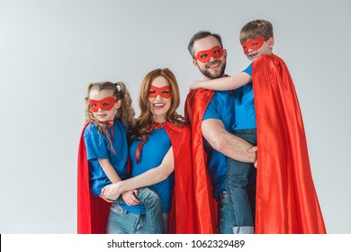 cheerful family of superheroes in masks and cloaks smiling at camera on grey - Powered by Shutterstock