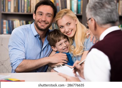 Cheerful family of three talking with psychologist. Psychologist taking notes. There are many books in psychologist office