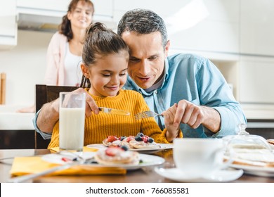 cheerful family together eating pancakes with berries at table on kitchen - Powered by Shutterstock