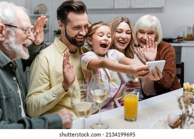 Cheerful Family Waving Hands During Video Call On Mobile Phone While Celebrating Easter