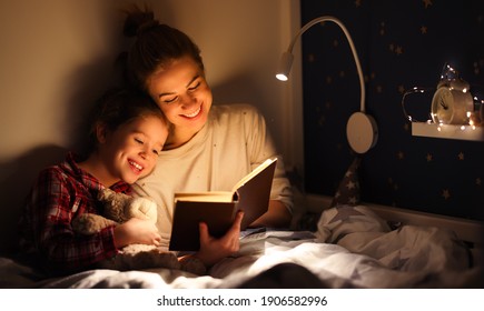 Cheerful Family: Woman And Girl Smiling And Reading Fairytale While Relaxing On Bed Near Lamp At Night At Home