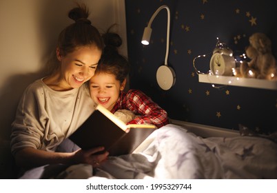 Cheerful Family: Woman And Girl Smiling And Reading Fairytale While Relaxing On Bed Near Lamp At Night At Home