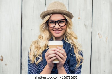 Cheerful fashionable blonde holding coffee outdoors on wooden background