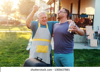 Cheerful Father In Law And Son In Law Hugging And Drinking Beer While Standing Next To Grill In Backyard. Family Gathering Concept.