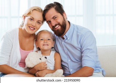 Cheerful father, mother and daughter sitting on the sofa in living room