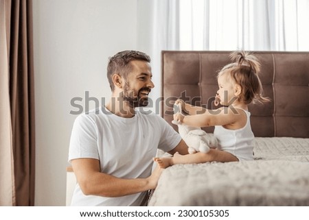 A cheerful father is playing with his baby girl while his daughter is showing him a toy and talking to him.