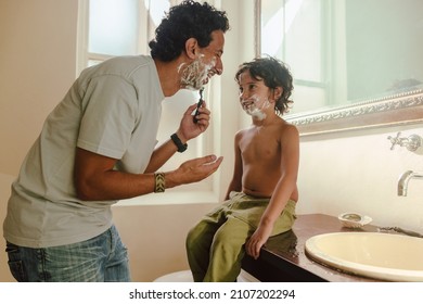 Cheerful father showing his son how to shave at home with shaving cream. Happy father teaching his son his shaving skills in the bathroom. Father and son spending some quality time together. - Powered by Shutterstock