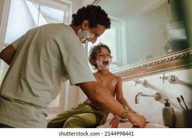 Cheerful father and son having fun with shaving foam in the bathroom. Father and son laughing happily with shaving cream on their faces. Loving father bonding with his young son at home.