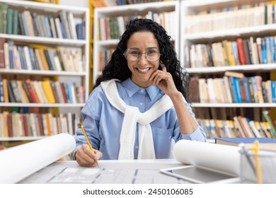 Cheerful female architect examining building plans in a library setting, smiling joyfully with bookshelves in the background. - Powered by Shutterstock