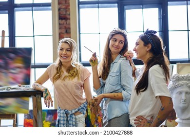 Cheerful Female Artists Smiling During Leisure Time In Art Studio Enjoying Collaborative Meeting Indoors, Happy Caucaisan Friends Spending Weekend In Gallery For Drawing And Creating Paintings