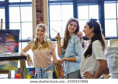 Cheerful female artists smiling during leisure time in art studio enjoying collaborative meeting indoors, happy Caucaisan friends spending weekend in gallery for drawing and creating paintings