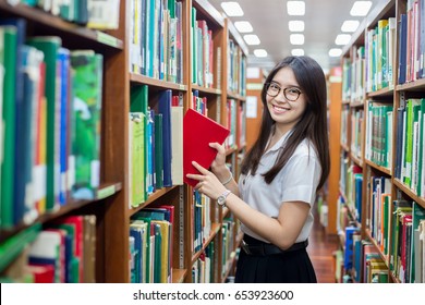 Cheerful female Asian student putting in order books returned after reading for literature lesson standing near bookshelves in modern interior library of university during break between lesson. - Powered by Shutterstock