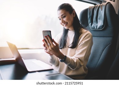 Cheerful female blogger working during trip on railroad sitting in train with wireless internet connection making picture on frontage mobile phone camera, happy woman posing for selfie on smartphone