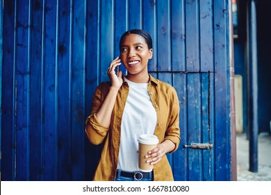 Cheerful female with caffeine beverage in hand enjoying friendly smartphone communication during leisure at loft urbanity, happy hipster girl making sincerely conversation via cellphone application - Powered by Shutterstock