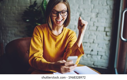 Cheerful Female In Classic Eyeglasses Happy With Received Email Message Using Cafe Internet Connection On Cellular Technology, Smiling Blogger Reading Online Reviews Browsed On Smartphone Device