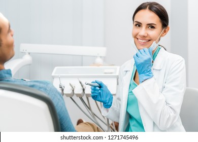 cheerful female dentist holding drill and smiling near patient  - Shutterstock ID 1271745496