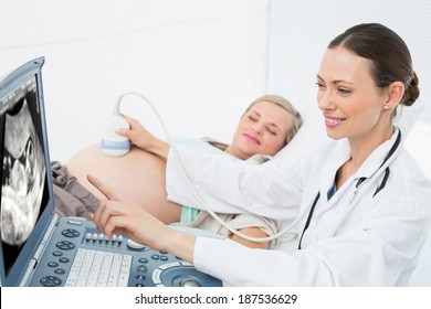 Cheerful female doctor showing woman her baby on ultrasound at the hospital