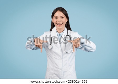 Cheerful female doctor with stethoscope pointing downwards with both hands, expressing excitement or highlighting something, set against clean blue background