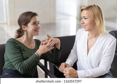 Cheerful female employees enjoying break. Two women in formal clothes sitting in office lounge, chatting and laughing. Informal talk concept