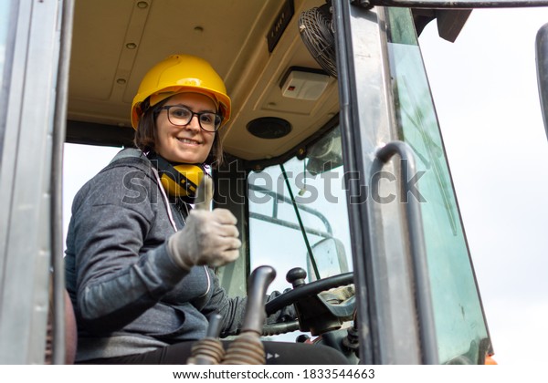 cheerful\
female excavator operator on construction site. Woman construction\
apprentice learning to drive heavy\
equipment