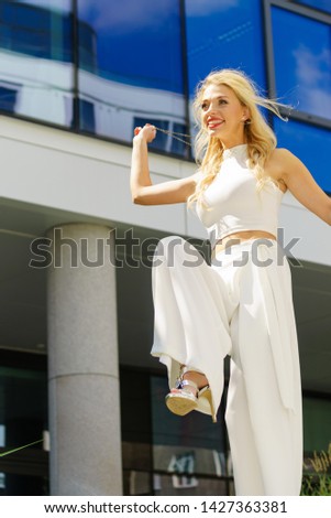 Cheerful female fashion model presenting casual elegant outfit. Woman holding purse bag having fun outdoor.