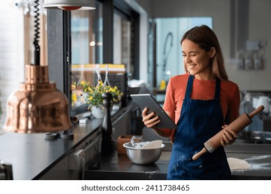 Cheerful female food blogger professional baker looking at digital tablet in commercial kitchen. Portrait of successful woman baker with digital tablet in pastry kitchen. - Powered by Shutterstock