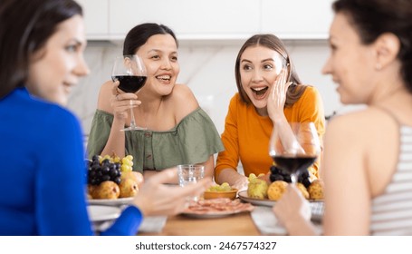 Cheerful female friends enjoying home gathering with wine and light snacks at kitchen table, engaging in lively conversations.. - Powered by Shutterstock