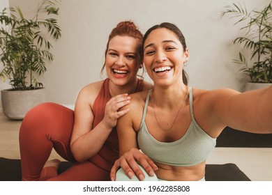 Cheerful female friends taking selife at yoga gym. Women in sports wear taking a break from workout and talking selfie at fitness studio. - Powered by Shutterstock