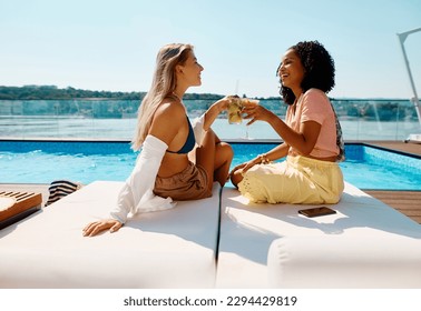 Cheerful female friends toasting with cocktails and having fun by swimming pool during summer day. Copy space.  - Powered by Shutterstock